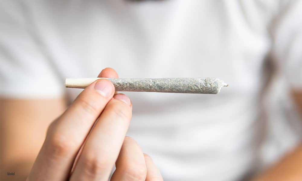 Close-up image of a person holding a cannabis joint